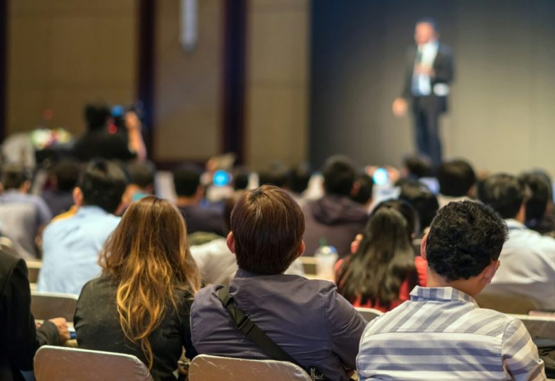 rear-side-of-audiences-sitting-and-listening-the-speackers-on-the-stage-in-low-light-conference-hall-1.jpg